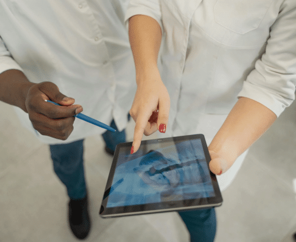 A pair of medical professionals looking and pointing at a tablet.