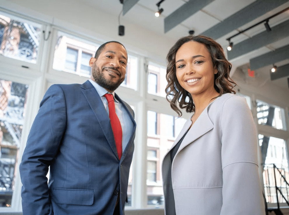 A business man and woman smiling inside a corporate building.