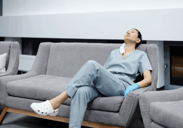 A nurse in scrubs sitting on a couch looking burned out.